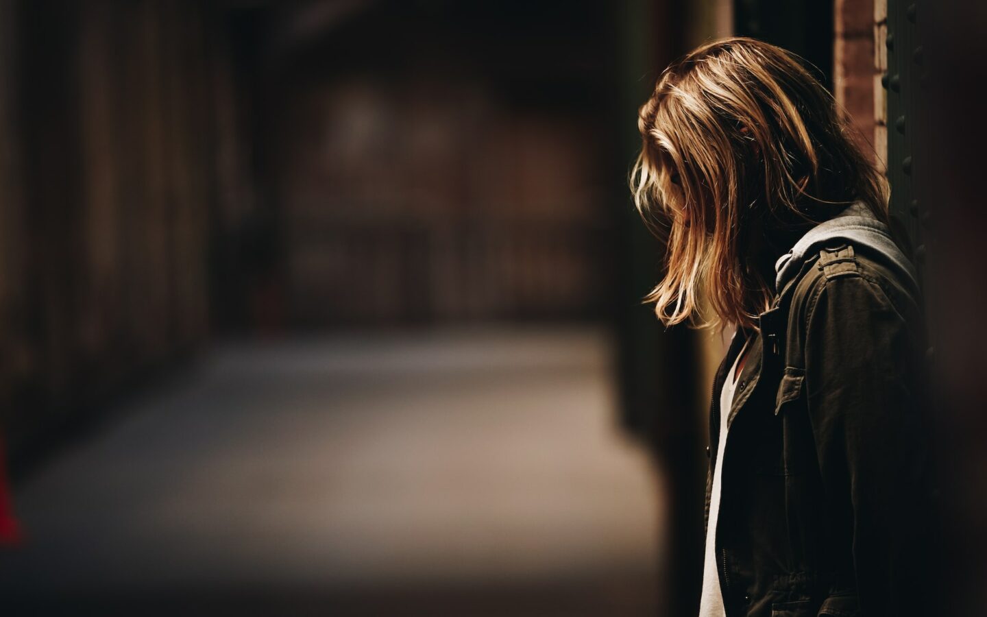 profile of scared young girl leaning against a wall, hair covering her face to promote safeguarding course